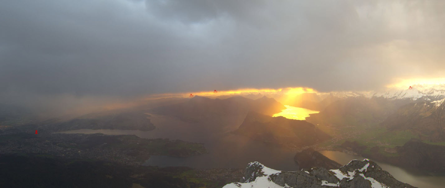Webcambild Pilatus am Morgen. Das Gersauerbecken im feurigen Morgenrot. Der Regen erfasste die Zentralschweiz pünktlich zu Tagesbeginn. (roundshot.ch)