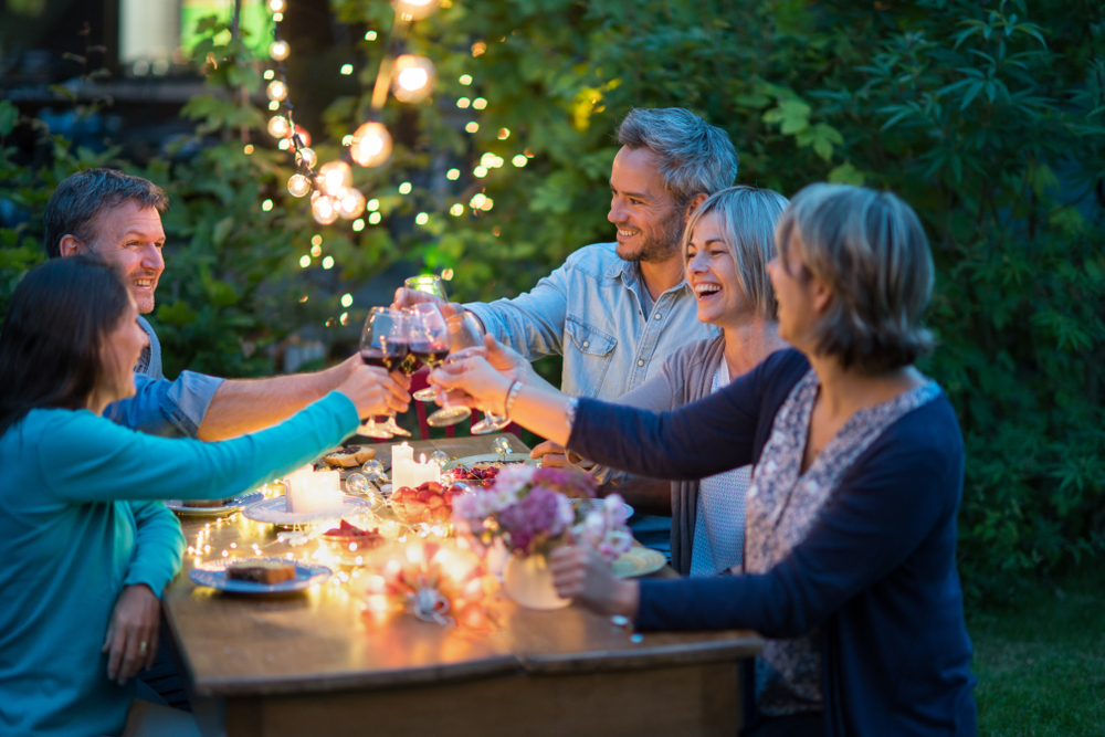 Leute sitzen im Garten am Tisch und stoßen mit Wein an.